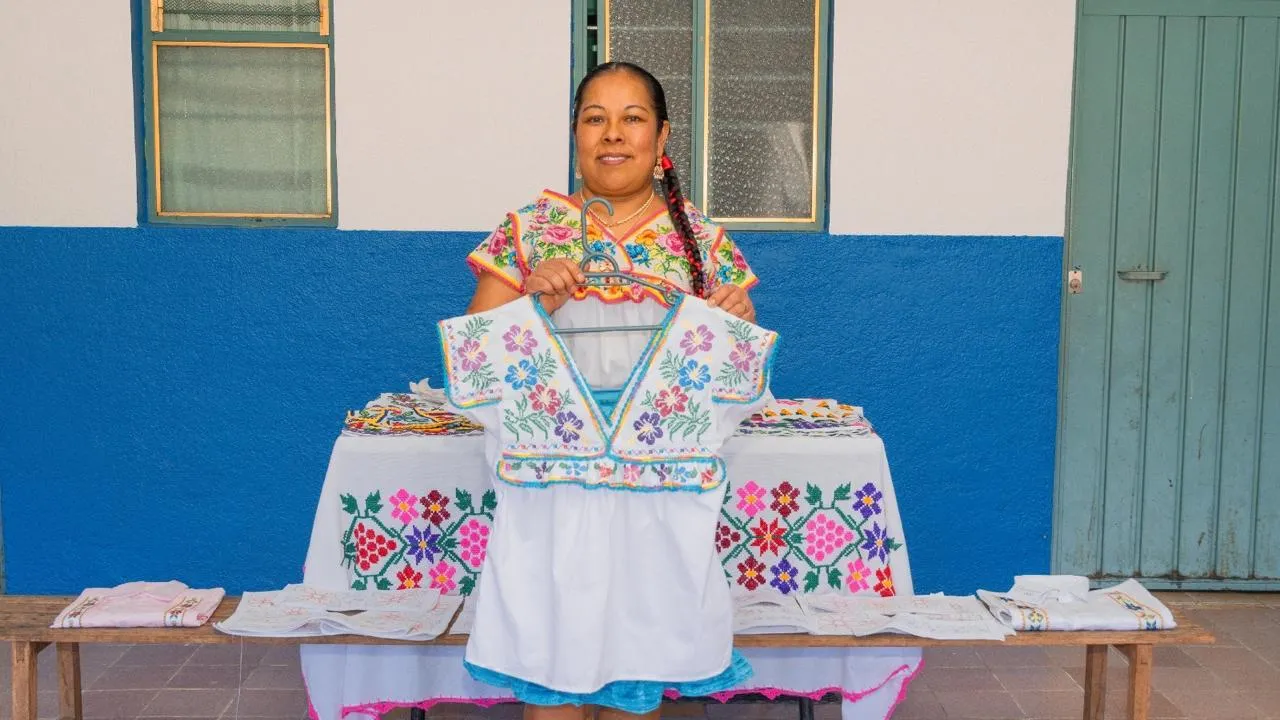 Artesana mostrando una blusa blanca con bordados coloridos típicos de Oaxaca